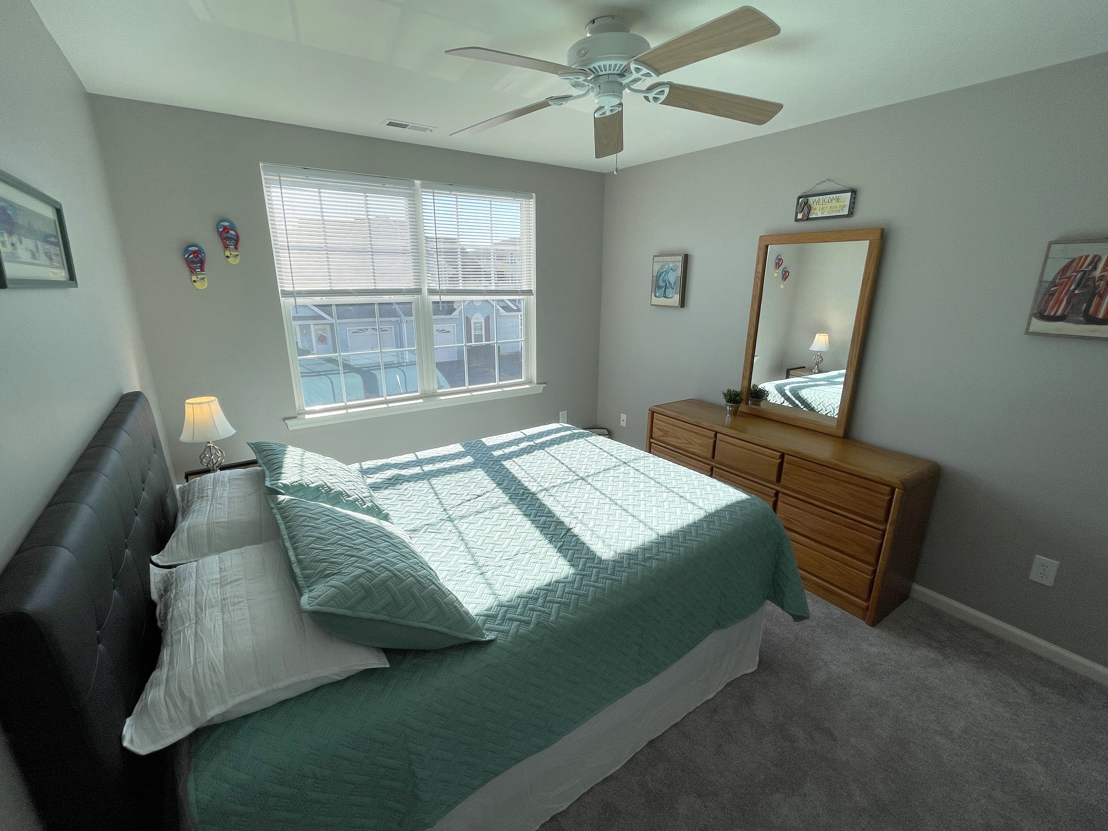 Une chambre à coucher comprenant un lit, une commode, un ventilateur de plafond, une fenêtre et une pancarte de bienvenue.