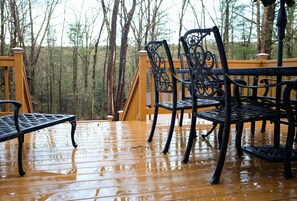 Eine Holzterrasse mit Metallstühlen und einer Bank, umgeben von Bäumen.