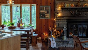 Ein gemütliches Blockhaus-Interieur mit einer Holzeinrichtung, einem Steinkamin und einem großen Fenster mit Blick auf einen Wald.