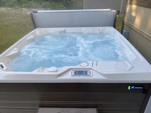 Un jacuzzi con panel de control y pantalla digital, rodeado por una terraza de madera y una valla de madera.