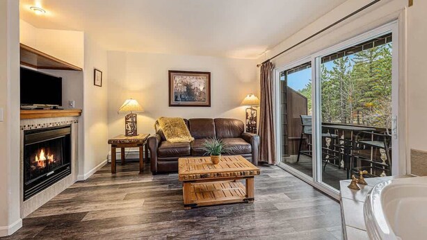 A living room with a fireplace, leather sofa, coffee table, and a large sliding glass door leading to an outdoor area. - Fall River Escape; Perfect Getaway on Fall River! (Estes Park)