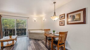 A room with a dining table, chairs, a chandelier, a bathtub, and a large window with a view of trees. - Fall River Escape; Perfect Getaway on Fall River! (Estes Park)