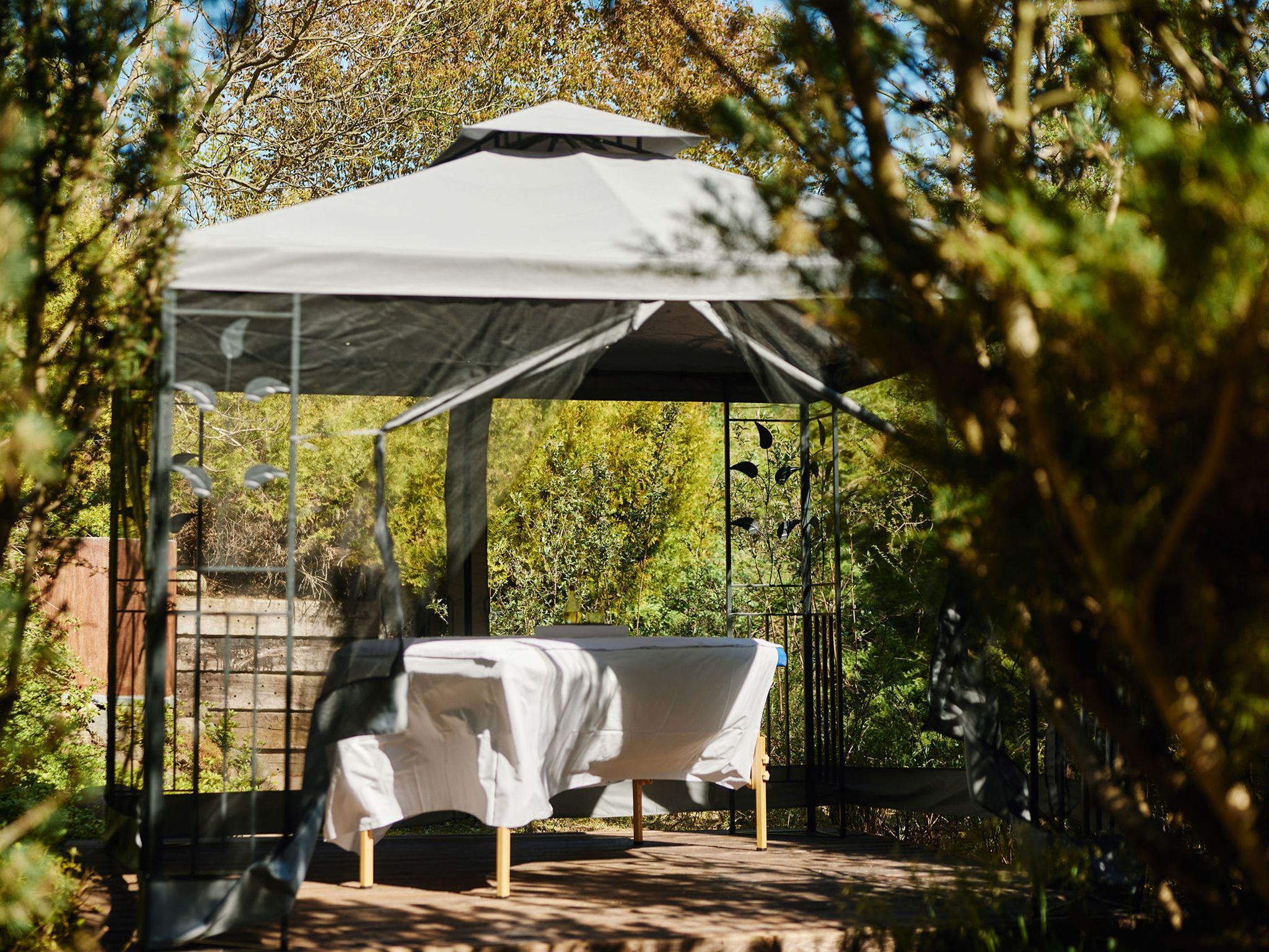 A gazebo with a bed inside, surrounded by trees.