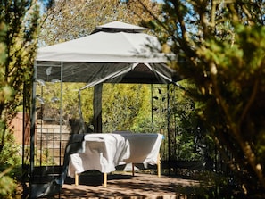A gazebo with a bed inside, surrounded by trees.
