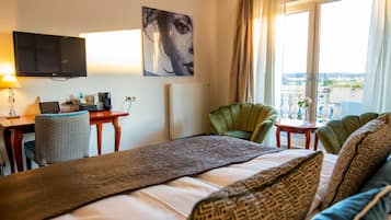 A hotel room with a bed, a desk with a computer, a television, a chair, and a view of the outdoors.
