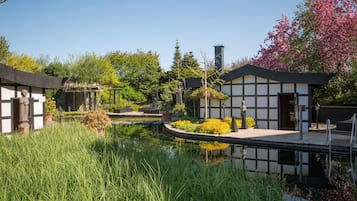 A traditional Japanese-style building with a koi pond, surrounded by lush greenery and flowering trees.
