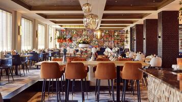 A spacious restaurant with high ceilings, modern bar seating, and a central dining area with a long table.