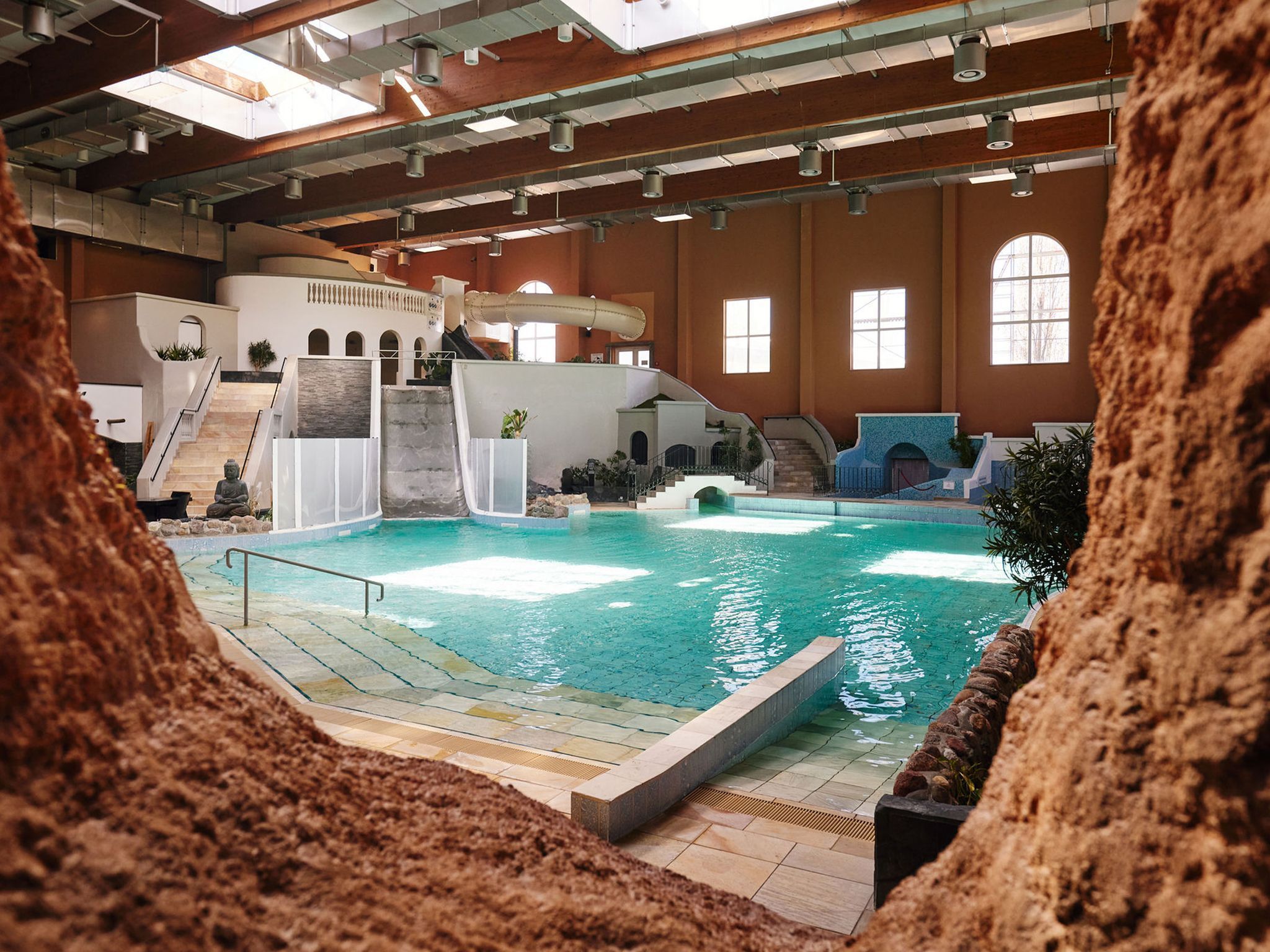 An indoor swimming pool with a slide, stairs, and a Buddha statue.