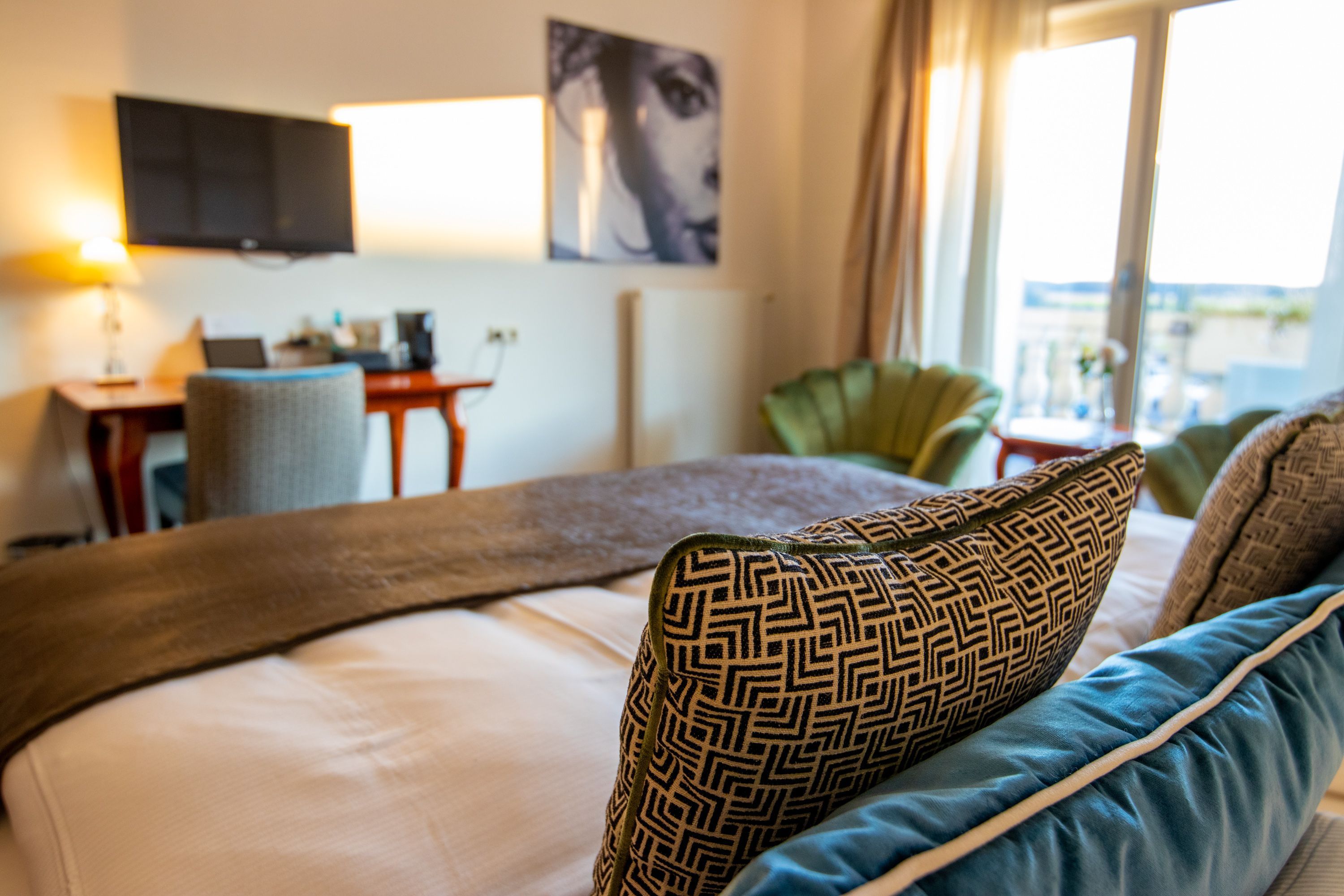 A hotel room with a bed, a desk with a laptop, a television, and a view of the outdoors.