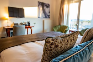 A hotel room with a bed, a desk with a laptop, a television, and a view of the outdoors.