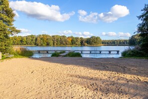 A sandy beach with a wooden dock extending into a lake, surrounded by trees. - Hotelzimmer - Van der Valk Resort Linstow Hotel (Dobbin-Linstow)