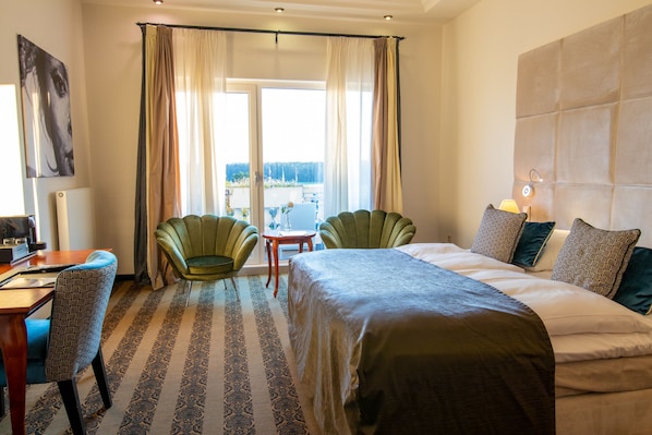 A hotel room with a bed, two chairs, a desk, a view through a window, and a headboard.