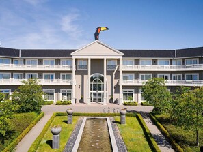 Ein mehrgeschossiges Gebäude mit einem zentralen Eingang, einem Brunnen und einem gepflegten Garten.