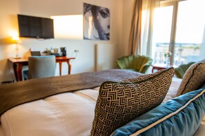 A hotel room with a bed, a desk with a laptop, a television, and a view of the outdoors. - Hotel Rooms - Van der Valk Resort Linstow Hotel   (Dobbin-Linstow)