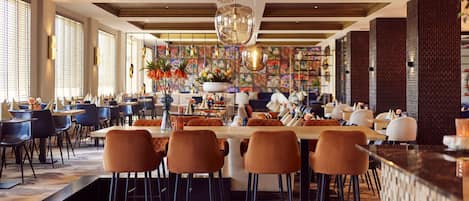 Un restaurante espacioso con techos altos, asientos de bar modernos y una zona de comedor central con una mesa larga.