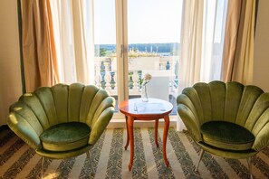 Dos sillones verdes orientados hacia un balcón con vista a un jardín y un edificio.