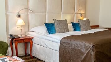 A hotel room with a bed, a bedside table with a lamp, a telephone, and a green chair.