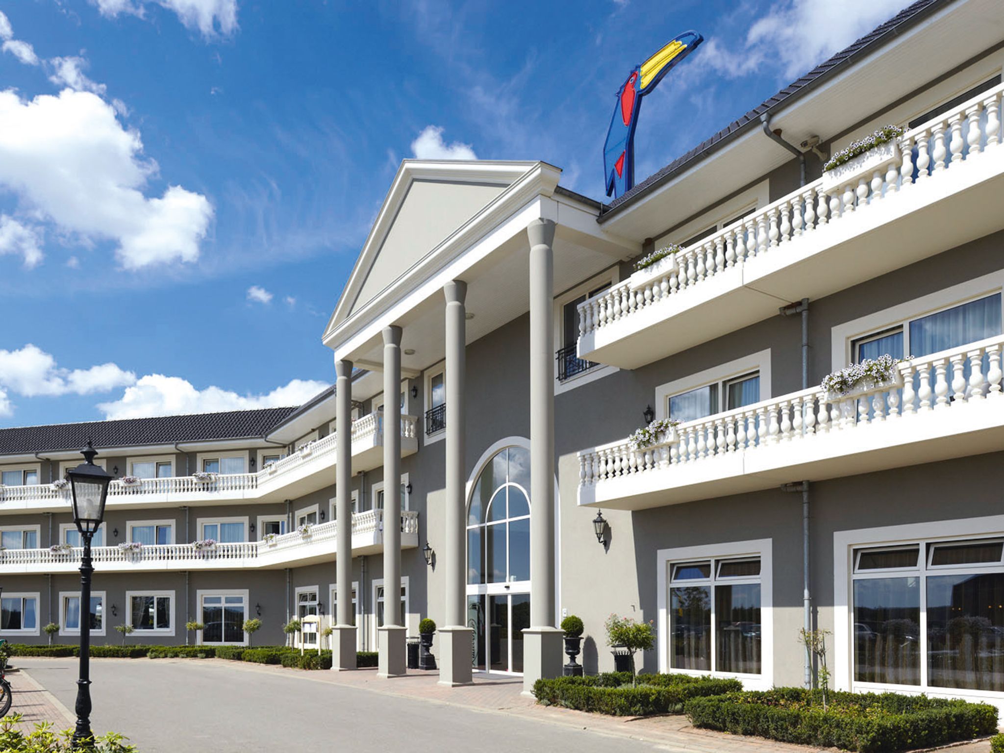 Een meerlaags hotel met een centrale ingang, balkons en een opvallend vogel logo op het dak.