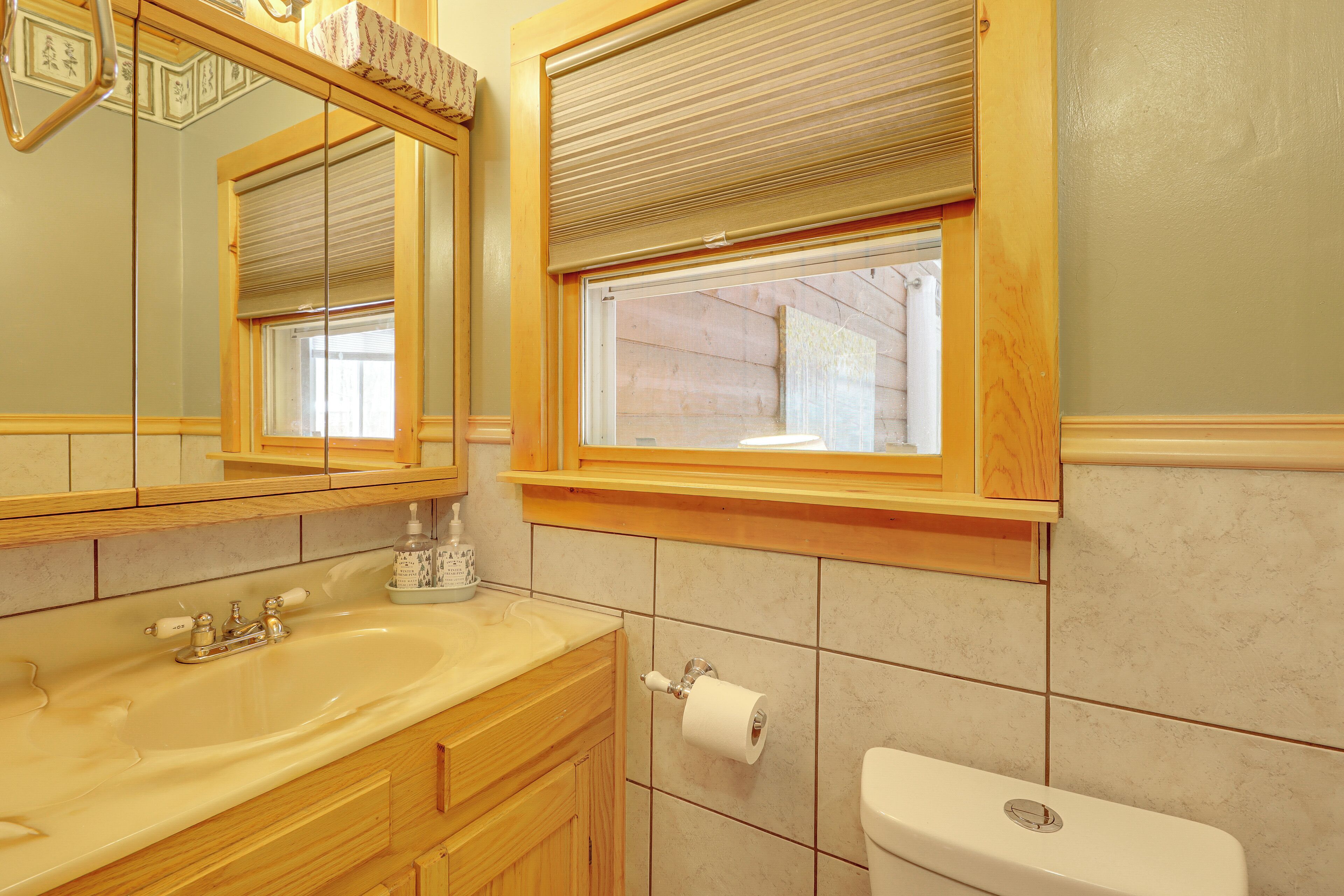 Een badkamer met een wastafel, spiegel, toilet en raam met zonwering.