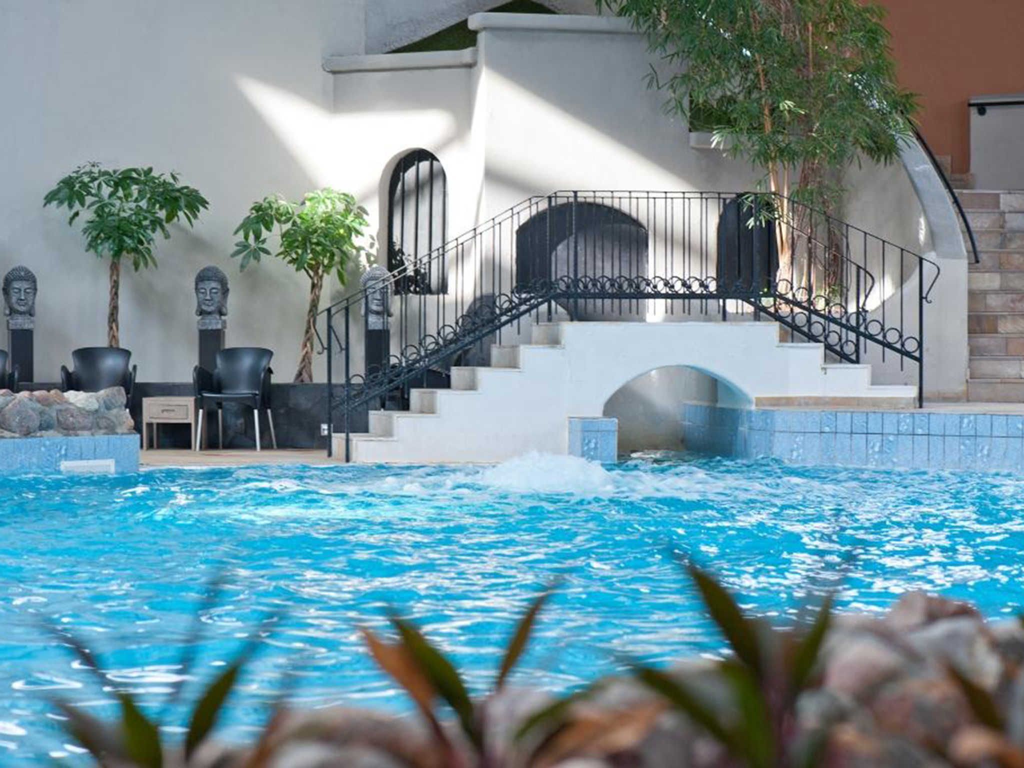 A swimming pool with a staircase leading to a covered area, surrounded by potted plants and stone features.