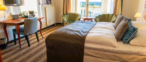 A hotel room with a bed, a desk with a laptop, a chair, a TV, and a view of the outdoors.