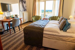 A hotel room with a bed, a desk with a laptop, a chair, a TV, and a view of the outdoors. - Hotel Rooms - Van der Valk Resort Linstow Hotel   (Dobbin-Linstow)
