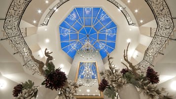 A grand atrium with a geometric blue ceiling, a central chandelier, and ornate metal railings.