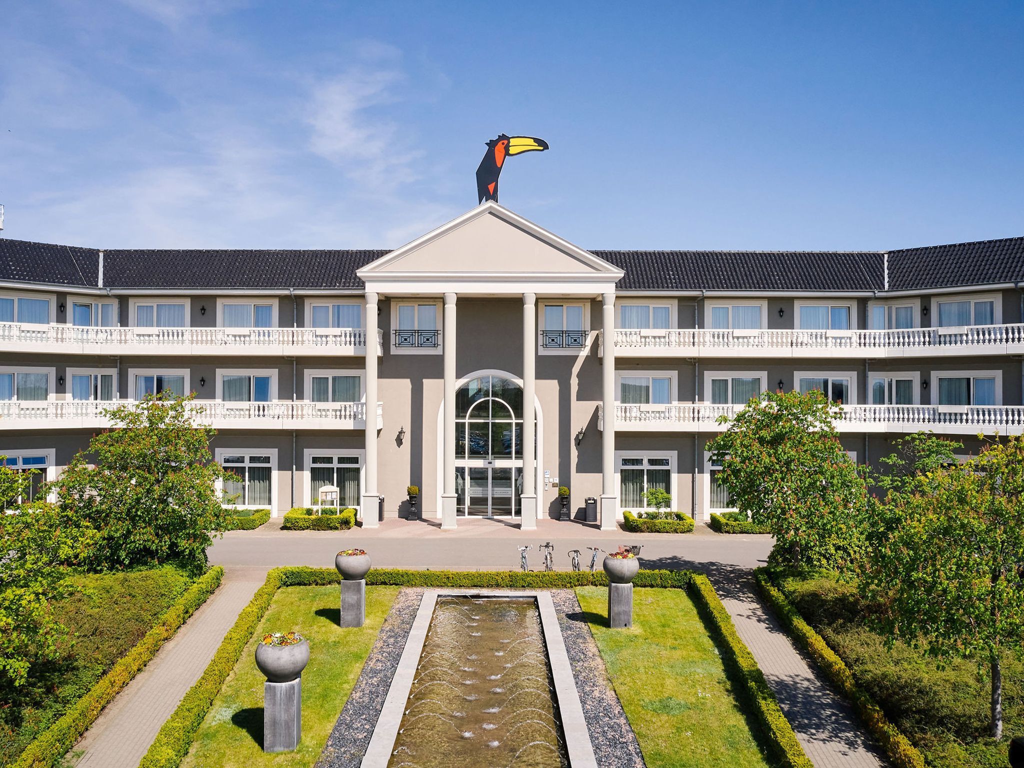 A multi-story building with a central entrance, a fountain, and a well-maintained garden.
