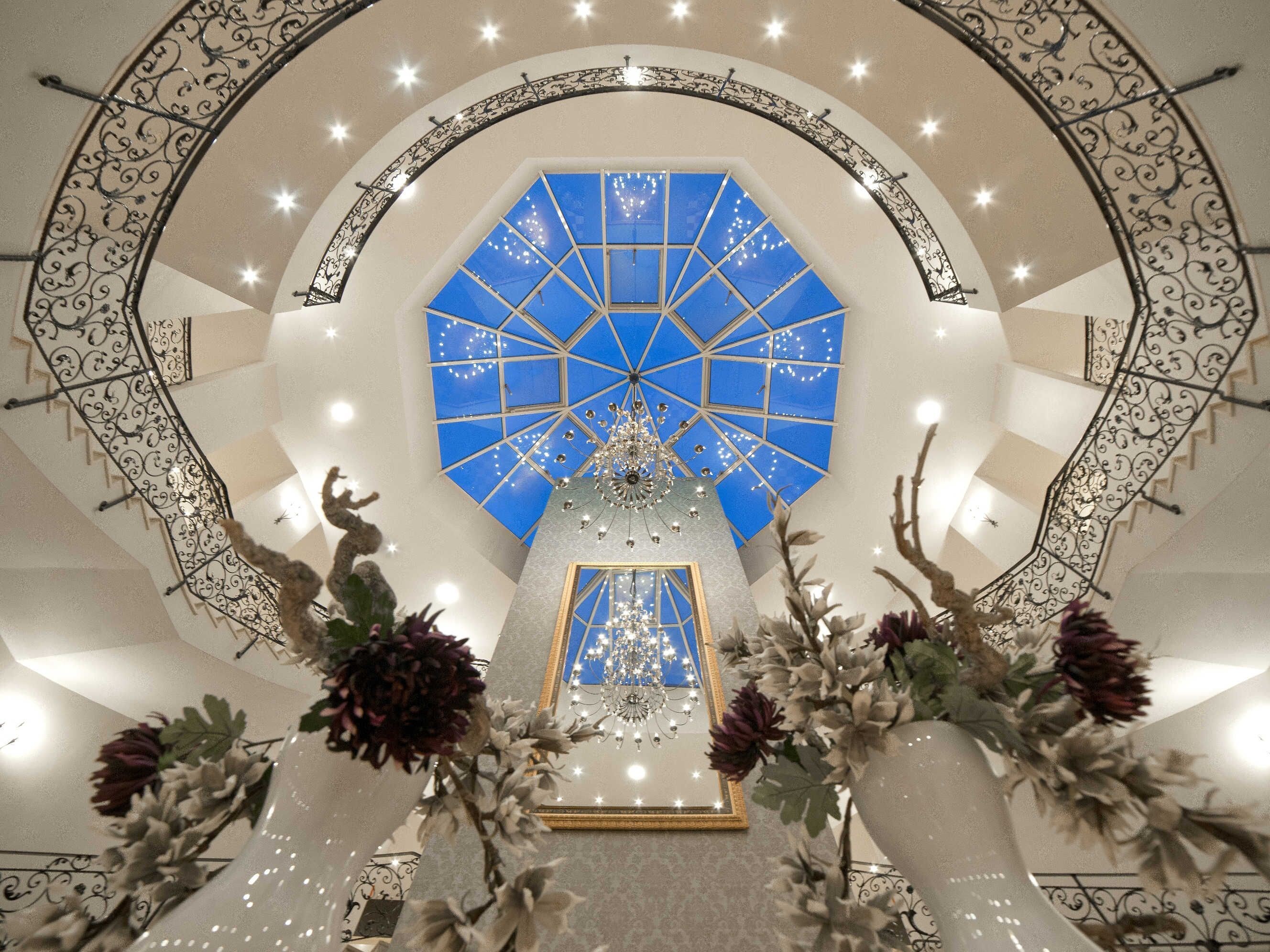 Ein beeindruckendes Atrium mit blauer, geometrischer Decke, einem zentralen Kronleuchter und aufwendigen Metallgitterläufungen.