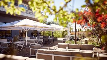 An outdoor seating area with tables and chairs, umbrellas, and a building in the background.