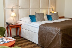 A hotel room with a bed, a bedside table with a lamp, a telephone, and a green chair. - Hotel room (a) - Van der Valk Resort Linstow Hotel (Dobbin-Linstow)