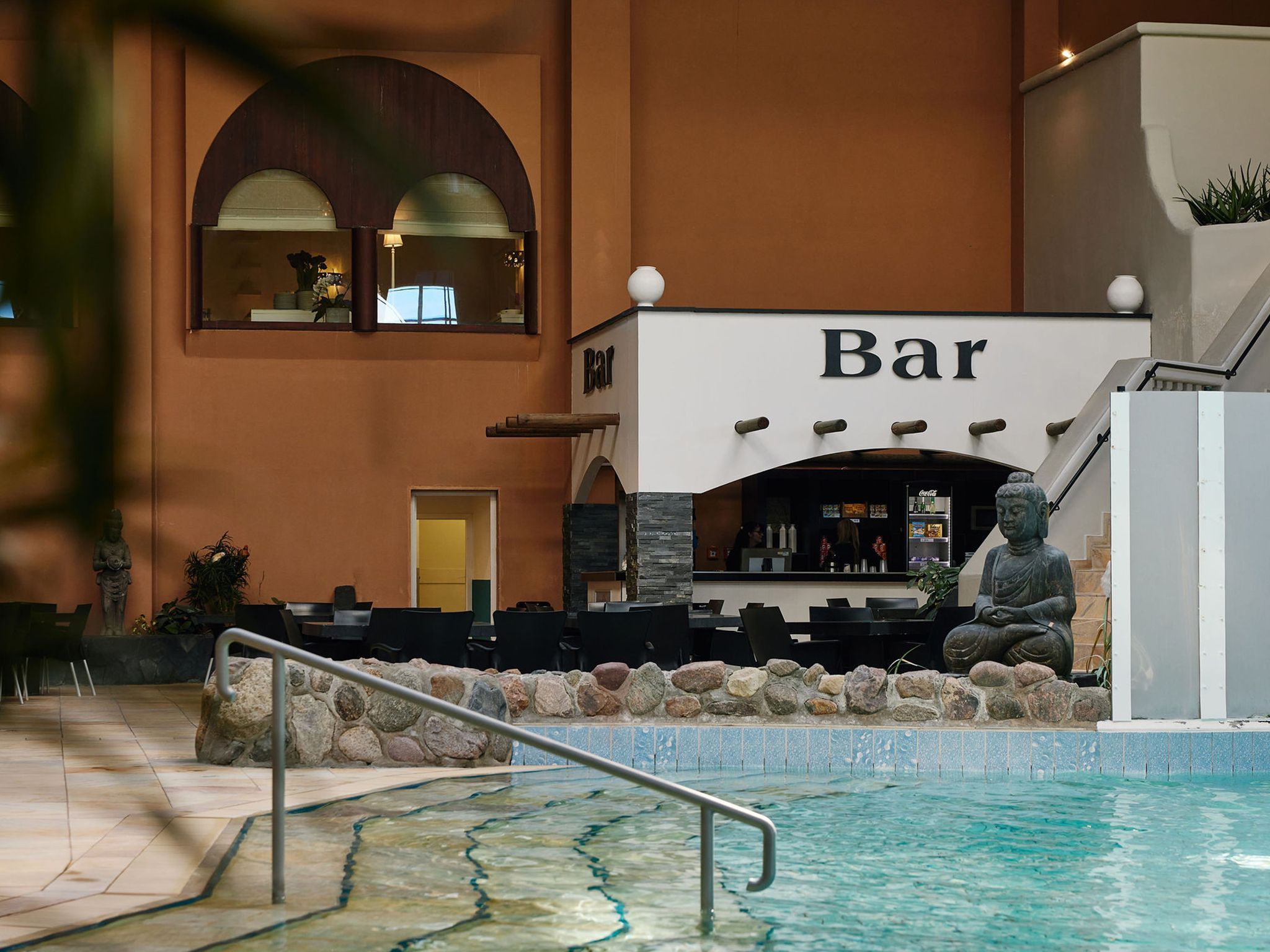 An indoor bar area with a pool, stone wall, and Buddha statue.