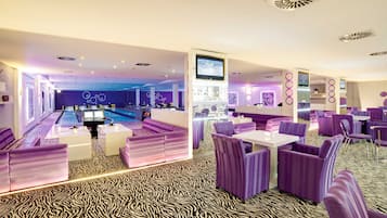 A modern lounge area with purple seating, a pool table, and a bar.