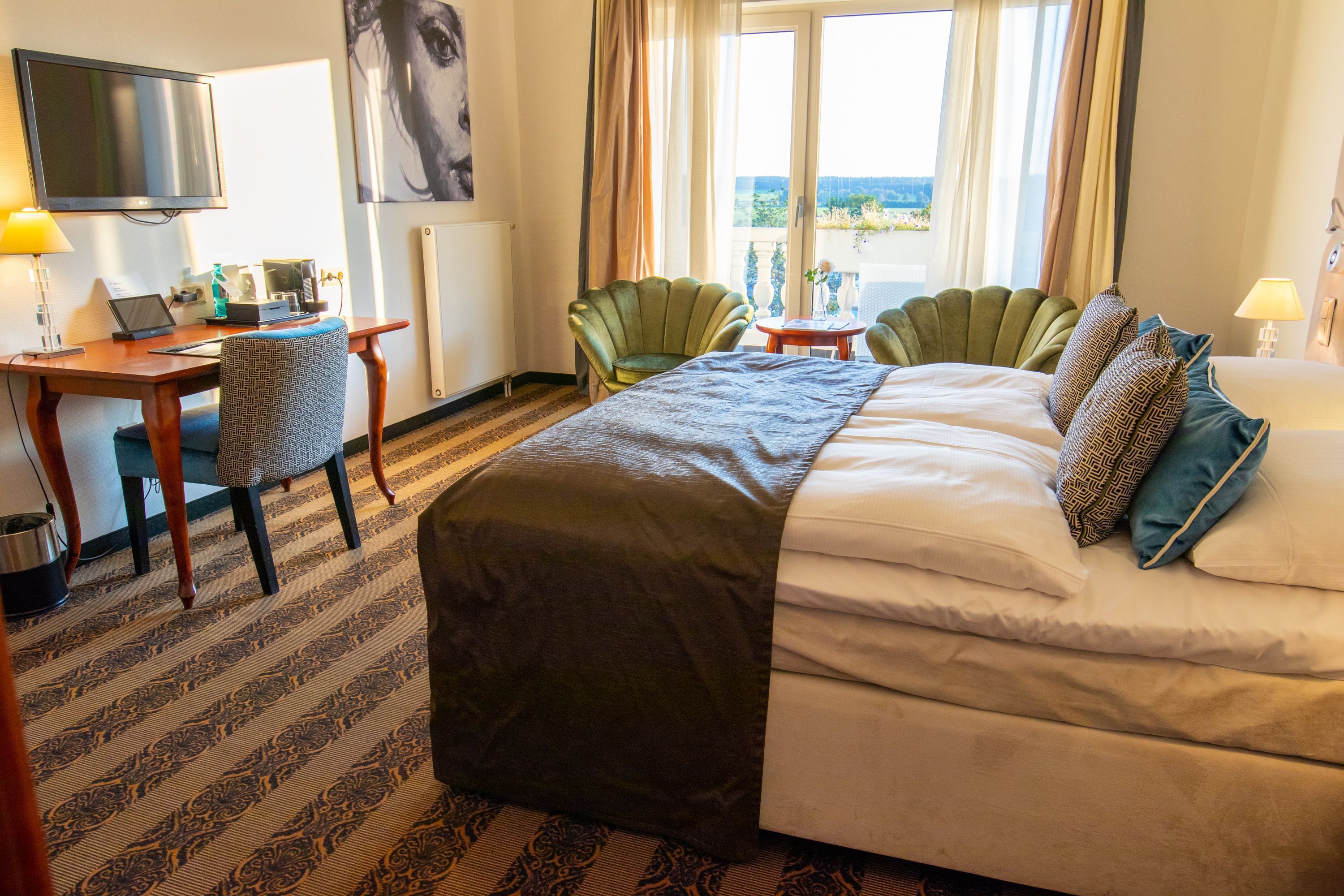 A hotel room with a bed, a desk with a laptop, a chair, a TV, and a view of the outdoors.