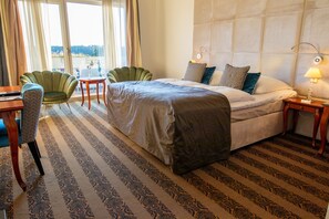 A hotel room with a bed, two chairs, a small table, a lamp, and a view through a window. - Hotel Room (a) - Van der Valk Resort Linstow Hotel   (Dobbin-Linstow)