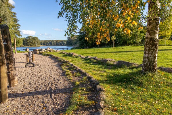 A gravel path leading to a bench by a lake, surrounded by trees and a grassy area.