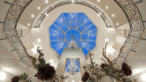 A grand atrium with a geometric blue ceiling, a central chandelier, and ornate metal railings. - Hotel room (a) - Van der Valk Resort Linstow Hotel (Dobbin-Linstow)