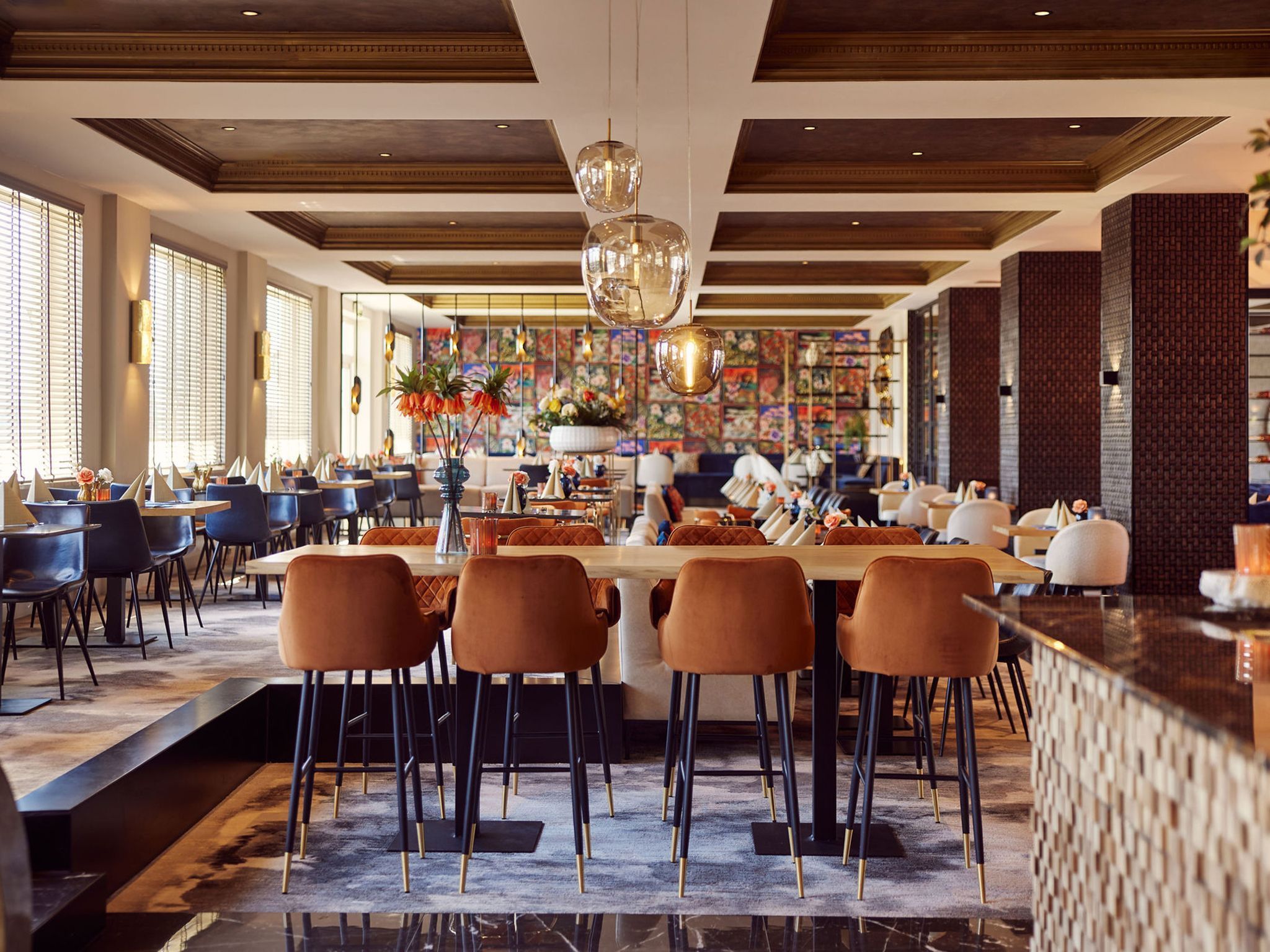 A spacious restaurant with high ceilings, modern bar seating, and a central dining area with a long table.