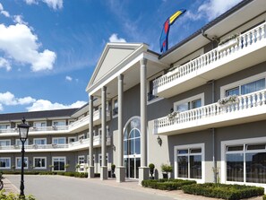 A multi-story hotel with a central entrance, balconies, and a distinctive bird logo on the roof. - Hotel Room (a) - Van der Valk Resort Linstow Hotel   (Dobbin-Linstow)