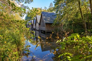 A row of wooden cabins with metal roofs, surrounded by dense foliage and a calm body of water.