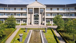 A multi-story building with a central entrance, a fountain, and a well-maintained garden. - Hotel room (a) - Van der Valk Resort Linstow Hotel (Dobbin-Linstow)