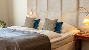 A hotel room with a large bed, two bedside lamps, a nightstand, and a green chair.
