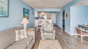 A living room with a sofa, armchair, and coffee table. There is a dining area with a table and chairs. The kitchen is visible in the background. - Oceanfront Myrtle Beach Condo with Resort Perks! (Myrtle Beach)