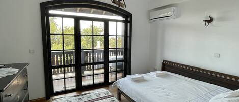 A bedroom with a bed, a dresser, a window with a view, and an air conditioning unit.