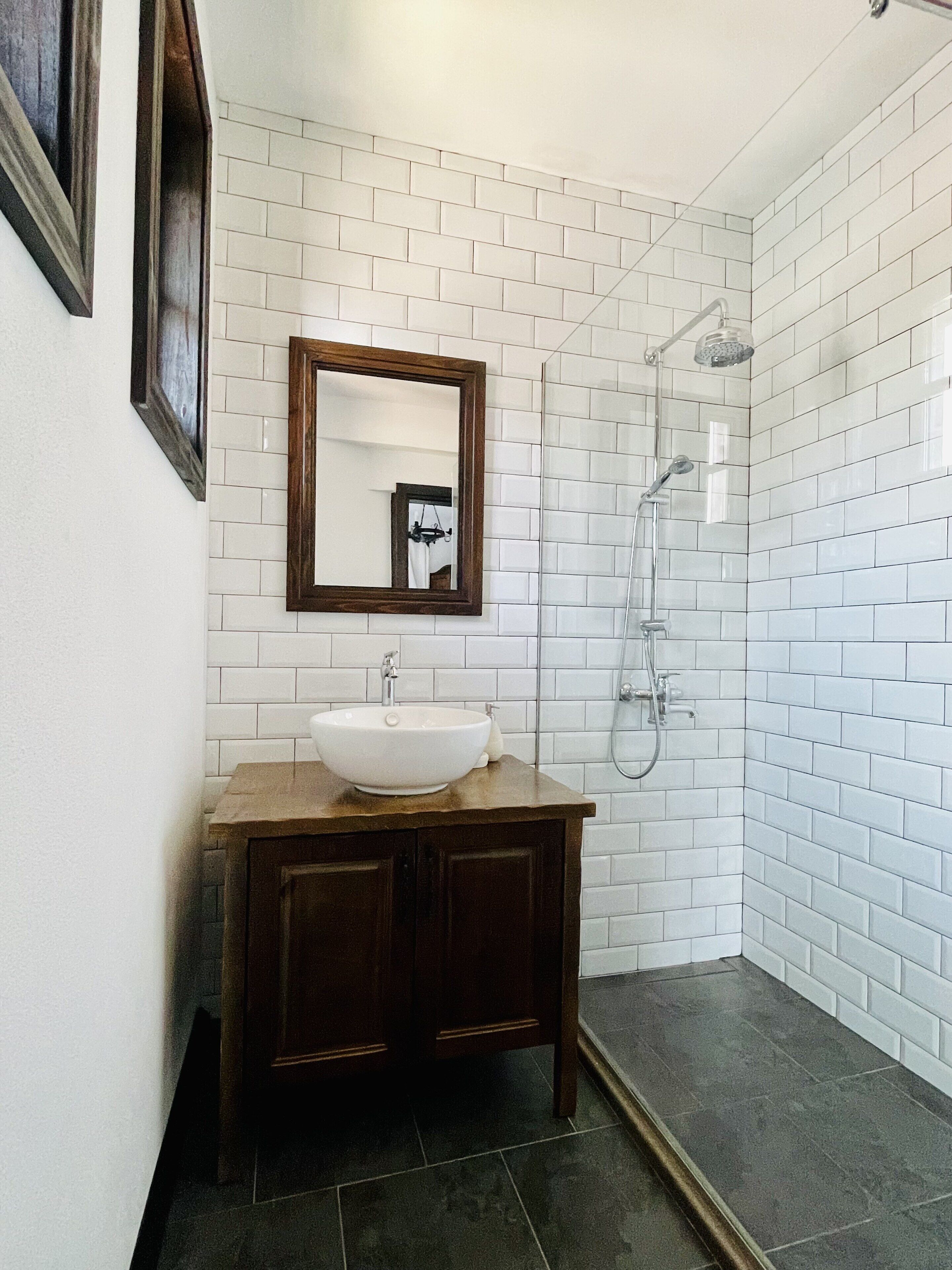 A bathroom with a white-tiled shower, a wooden vanity with a white sink, and a mirror above the vanity.