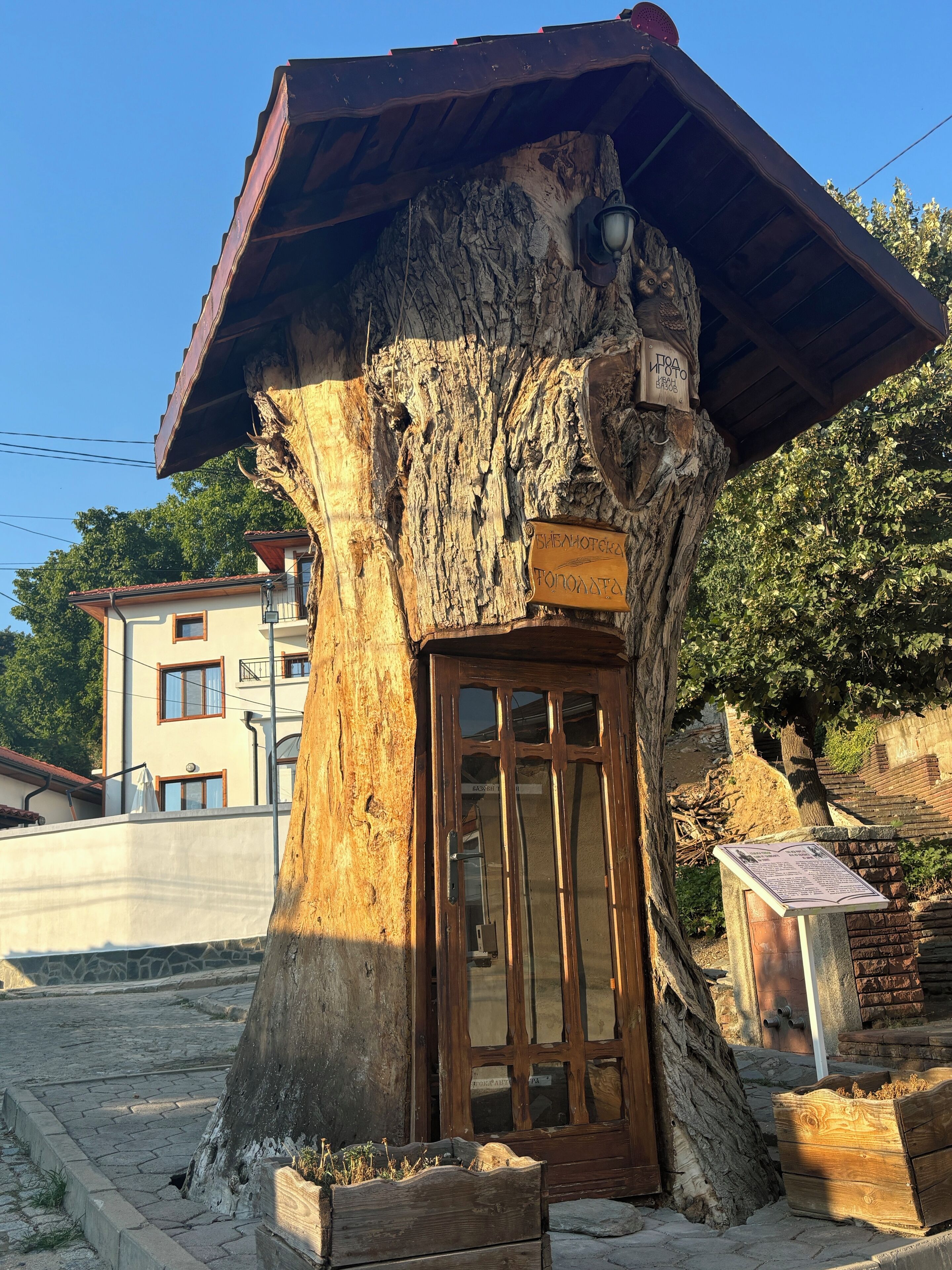 A rustic wooden structure with a door, surrounded by a stone wall and a paved area.