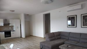 Un saló modern amb un sofà gris i una taula baixa, una cuina amb armaris blancs i forn encastrat, i dos quadres penjats a la paret.