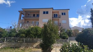 Un edifici residencial de dues plantes amb balcons, un mur de pedra i vegetació circumdant.