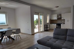 A spacious living area with a grey sofa, a dining table with chairs, and a kitchen in the background.