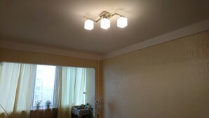 Una stanza con una lampada a sospensione, una finestra con tende e una ventola.